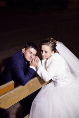 A bride and groom are sitting on a bench, the bride is wearing a white dress