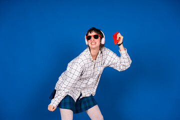 Young woman dancing and listening to music with headphones and smartphone on blue background