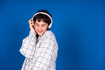 Fototapeta premium Young woman enjoying music with headphones on blue background