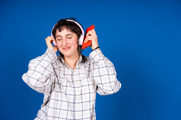 Young woman enjoying music with headphones and smartphone on blue background