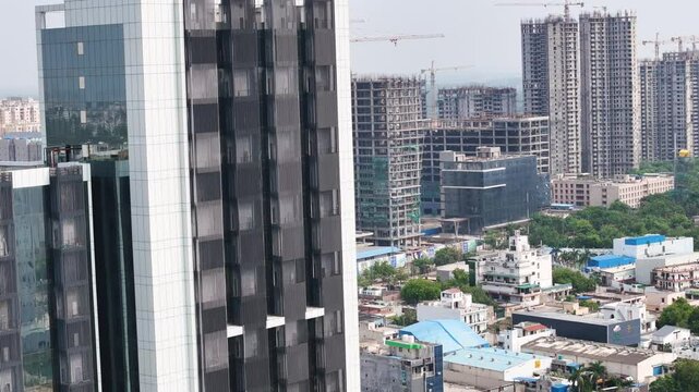 Aerial drone shot capturing reflections of the sky and cityscape on the facade of a tall glass building.