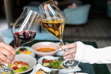Two people clinking red and white wine glasses over a table with gourmet dishes in a cozy restaurant, capturing a joyful celebration or dining moment.