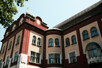 Obraz premium Close-up of Subotica City Hall, showcasing red and beige facade with ornate window frames and architectural details on a sunny day. Serbia country.
