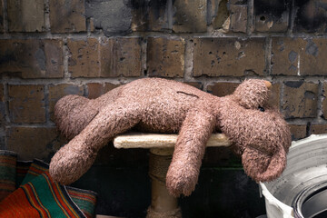 An old dirty teddy bear lies among the trash