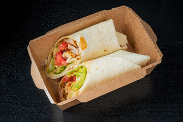 Two tortillas filled with grilled chicken, lettuce, and tomato are served in a stylish container