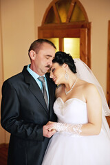 A bride and groom are embracing each other with a bouquet of flowers in between them. Scene is...