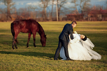 A bride and groom are kissing in front of a wooden well. The bride is wearing a white veil and the...