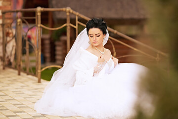 A woman in a white wedding dress sits on a swing, holding a bouquet of flowers. The scene is...