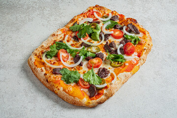 Freshly baked rectangular pizza adorned with vibrant veggies and savory beef on a textured surface