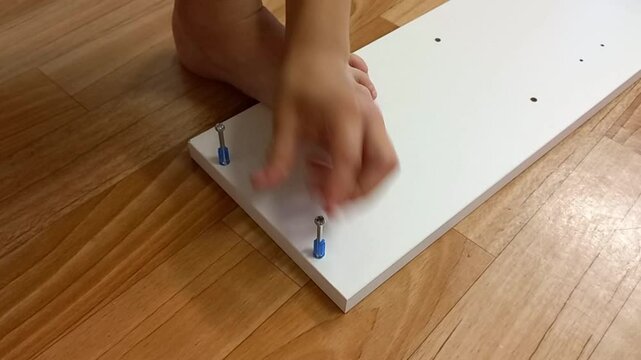 Child assembling furniture with hands on wooden floor at home  