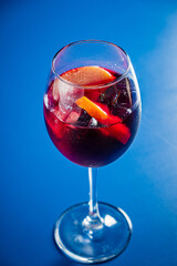 A colorful glass of fruity drink with apple and orange slices on a blue background