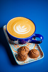 Rich coffee with intricate latte art accompanied by delicious cookies rests on a colorful plate