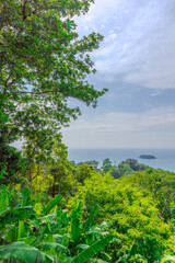 Views through lush green trees and palms over looking Kata and Kata Noi on the beautiful island of phuket in Thailand with lush green mountains and turquoise blue waters of the Andaman Sea