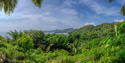Views through lush green trees and palms over looking Kata and Kata Noi on the beautiful island of phuket in Thailand with lush green mountains and turquoise blue waters of the Andaman Sea