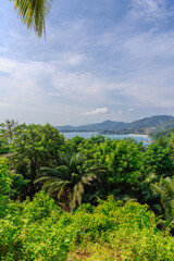 Fototapeta premium Views through lush green trees and palms over looking Kata and Kata Noi on the beautiful island of phuket in Thailand with lush green mountains and turquoise blue waters of the Andaman Sea