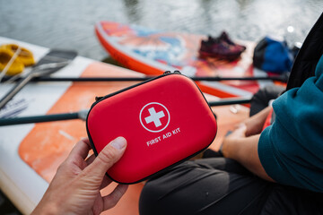 A person is holding a first aid kit in front of a paddle board