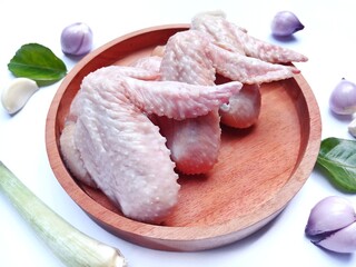 Fresh raw chicken wings on  wooden tray and some ingredients like shallots, garlic,lemon grass and...