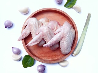 Fresh raw chicken wings on  wooden tray and some ingredients like shallots, garlic,lemon grass and...
