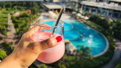 Pink smoothie in hand by the pool