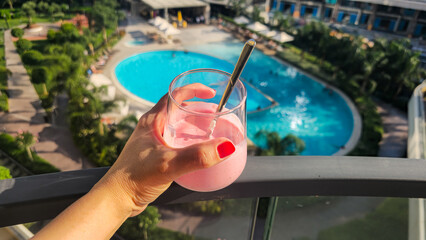 Pink smoothie in hand by the pool