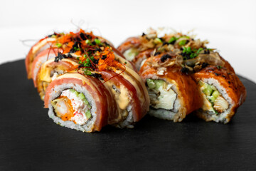 Assorted sushi rolls on a black slate board with creamy and crispy toppings, combining textures and colors in an elegant display.