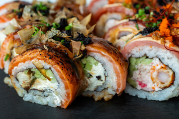 Assorted sushi rolls on a black slate board with creamy and crispy toppings, combining textures and colors in an elegant display. © Nestudio