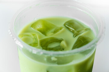 Macro shot of green ice cubes in a matcha latte inside a clear plastic cup. Minimalist style with a refreshing, cool mood.