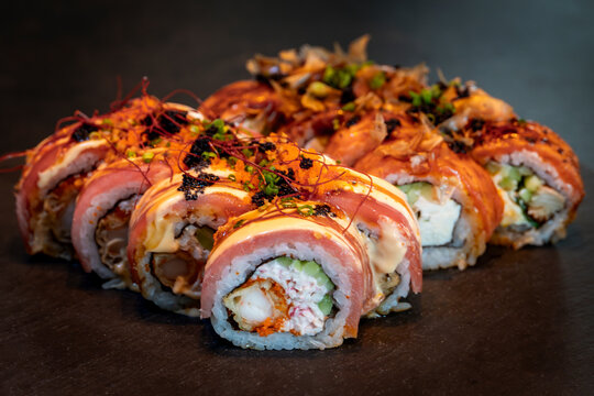 Assorted sushi rolls on a black slate board with creamy and crispy toppings, combining textures and colors in an elegant display.