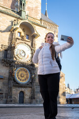 Mujer feliz paseando por el centro de Praga, tomandose una selfie con el reloj astronómico de fondo