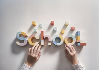 Hands arranging the word SCHOOL from colorful geometric shapes against the solid white background. Back to school, educational flat lay. 
