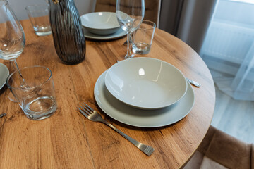 A beautifully crafted wooden table adorned with vibrant plates, colorful bowls, crystal glasses, and shiny silverware on its polished surface creates an inviting dining atmosphere