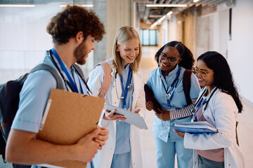 Happy students using digital tablet in hallway at medical university.