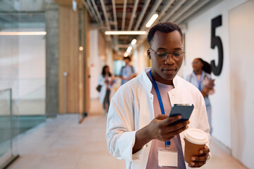 Black doctor student using cell phone in university hallway.