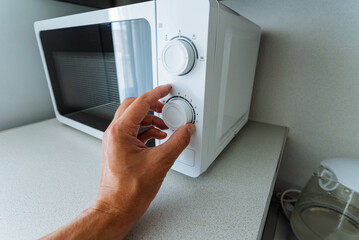An individual is currently pressing a button on a modern microwave, which is a common kitchen...