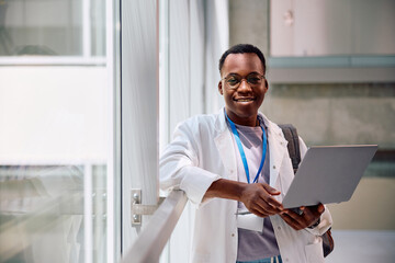 Happy black medical student with laptop at university looking at camera.