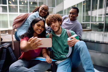 Happy diverse students taking selfie with cell phone at university campus.