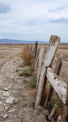 Weathered Wooden Fence Decaying Over Dry Farmland Under Overcast Sky
