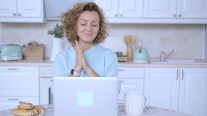 Cheerful female freelancer clapping hands in delight, enjoying a moment of satisfaction while working on a laptop in a cozy kitchen, savoring breakfast and a cup of coffee