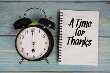 A Time for Thanks text written on notepad with alarm clock on wooden background