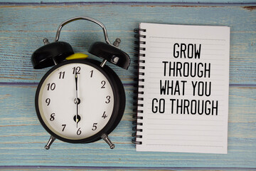 Grow Through What You go Through text written on notepad with alarm clock on wooden background