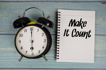 Make It Count text written on notepad with alarm clock on wooden background