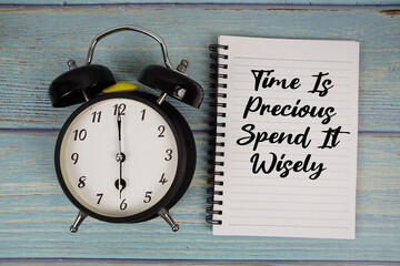 Time is Precious Spend It Wisely text written on notepad with alarm clock on wooden background