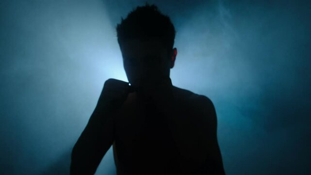 Young man throwing punch into camera in dark cinematic lighting, silhouette fight in blue moody atmosphere.