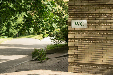 A restroom facility marked with a 'WC' sign is situated beside a winding pathway in a park. The...