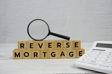 Reverse Mortgage alphabet letters with calculator and magnifying glass on wooden background