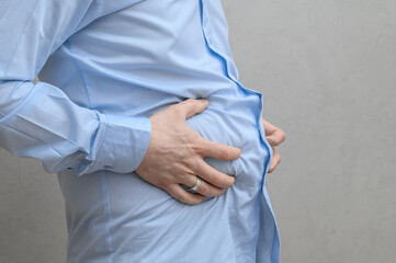 Slim man holds his hands to his swollen belly, severe painful indigestion, abdominal obesity