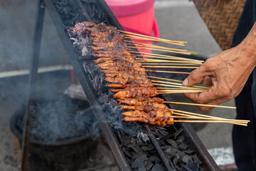 Hand Turning Delicious Marinated Chicken Satay on a Traditional Grill