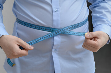 Fat man measures the circumference of his round belly, overweight and obesity
