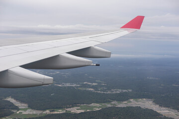 Fototapeta premium Commercial Airplane in Flight – Detailed Wing and Engines with Scenic Farmland and Forests Below, Captured Through Passenger Window
