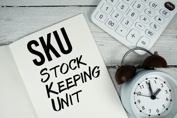 SKU Stock Keeping Unit text on paper notebook page with alarm clock and calculator on wooden...
